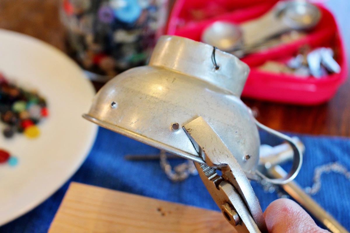 A vintage funnel being held with a pair of pliers, with holes punched in the side.