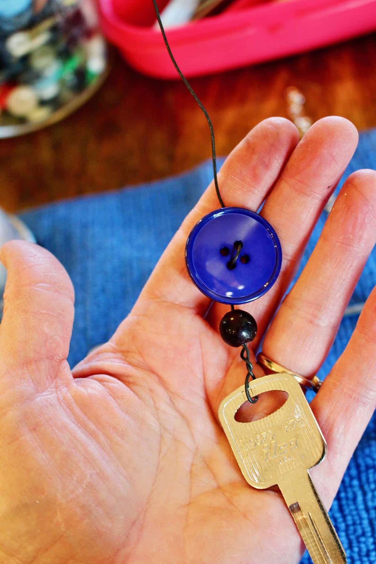 A hand holding a vintage key, a button, and a bead strung on a wire.