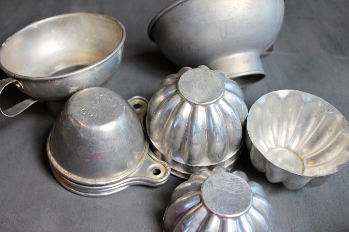 Stacks of vintage aluminum measuring cups, jello molds, funnels, and other kitchen items.