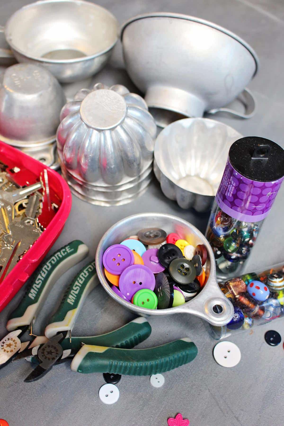 Vintage aluminum measuring cups and other kitchen items, an assortment of buttons, and other tools.