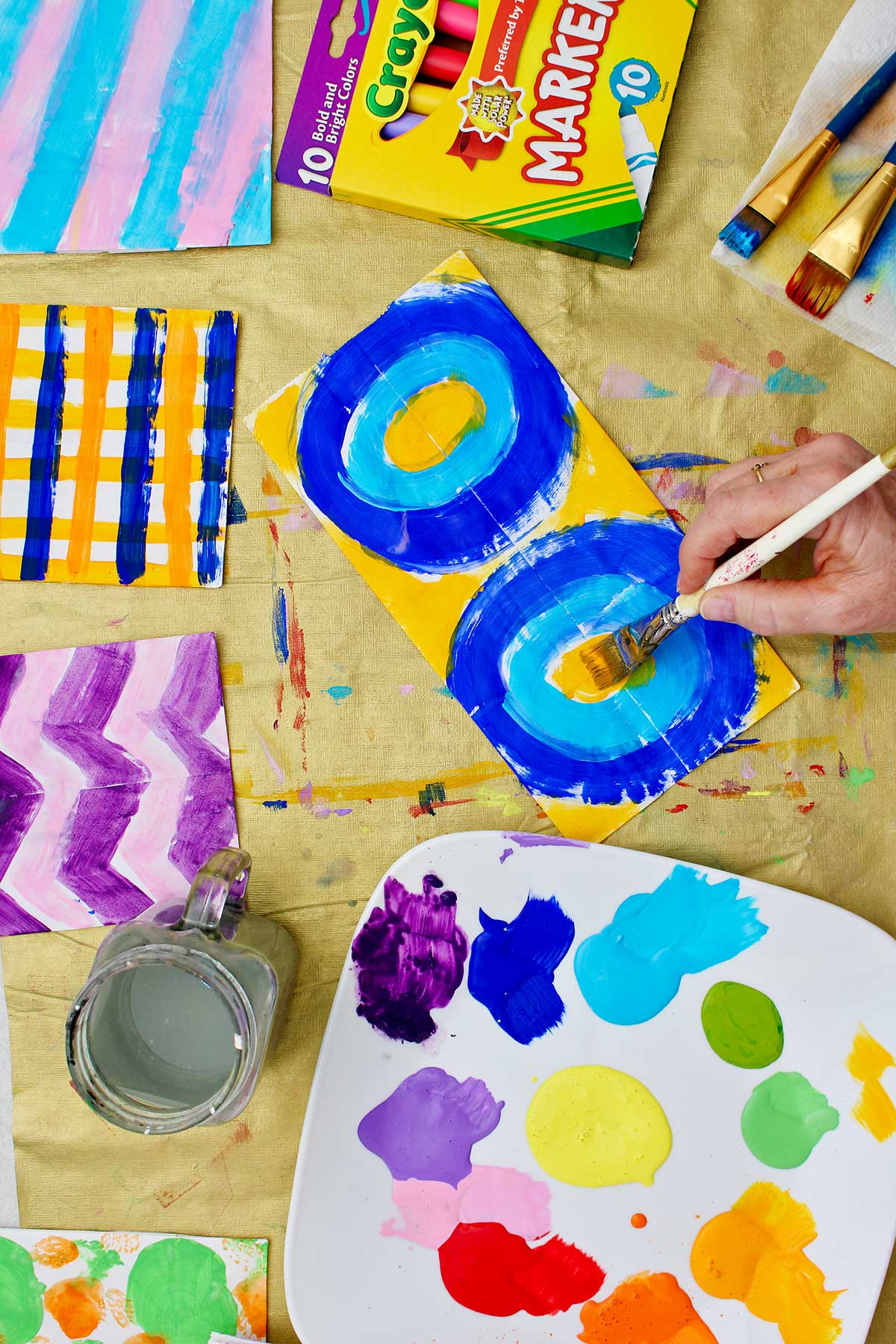 Person painting a paper bag with a circle pattern in orange and blue.