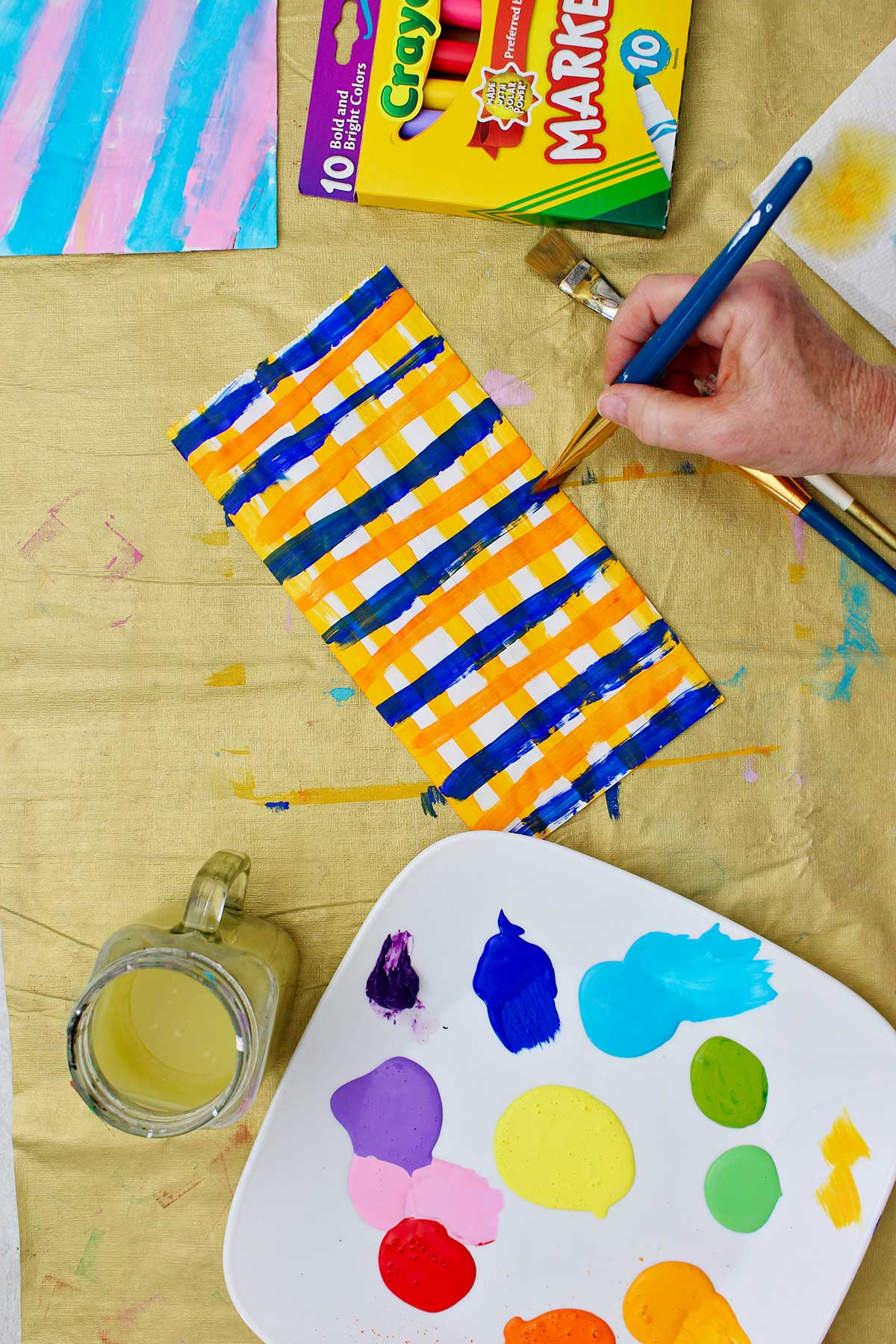 Person painting a paper bag in a plaid design orange and blue.