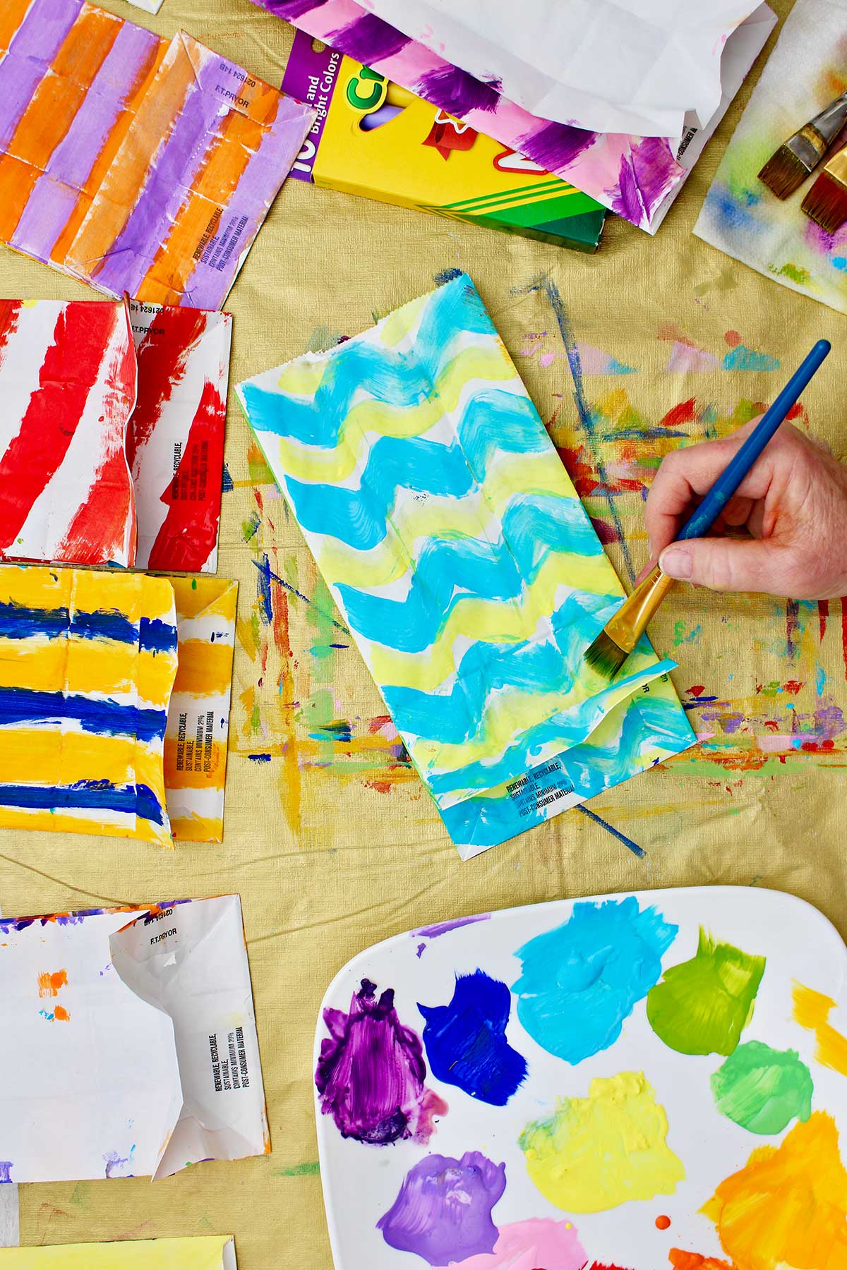 Person painting a paper bag in aqua and lime green chevron.