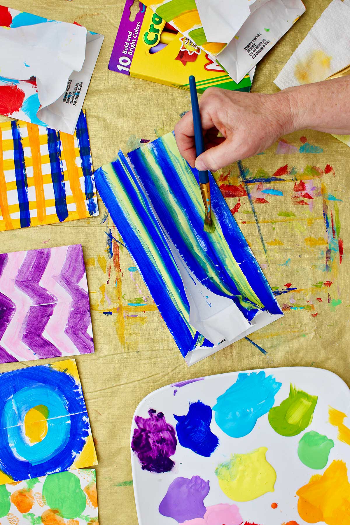 Person painting a paper bag with blue and green stripes.