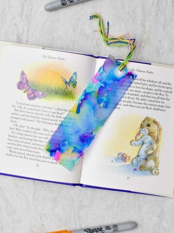 Completed colorful plastic bookmark resting in an open children's story book with colorful sharpies near by.