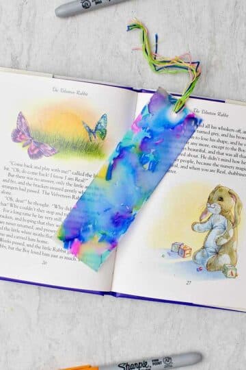 Completed colorful plastic bookmark resting in an open children's story book with colorful sharpies near by.