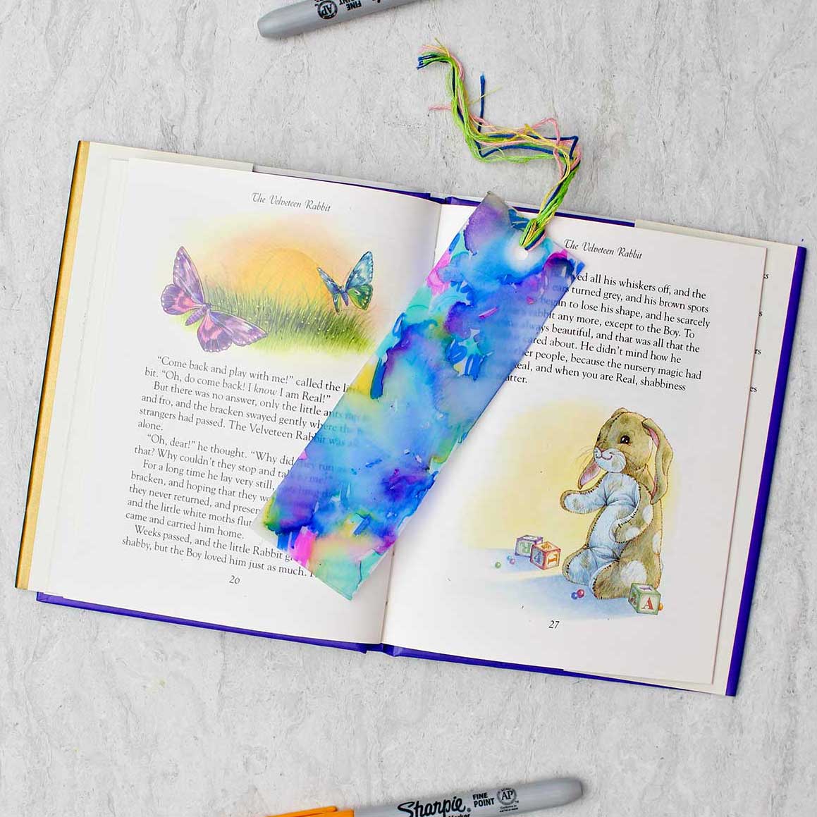 Completed colorful plastic bookmark resting in an open children's story book with colorful sharpies near by.