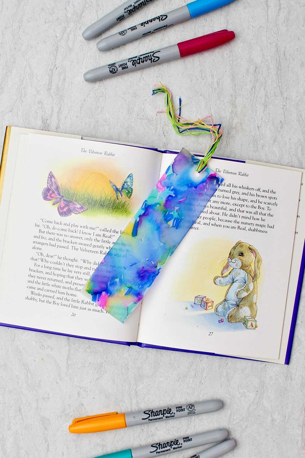 Completed colorful plastic bookmark resting in an open children's story book with colorful sharpies near by.