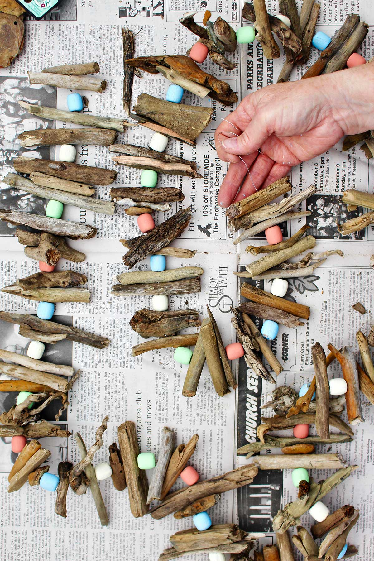 Person threading wire through pieces of driftwood and painted wooden beads.