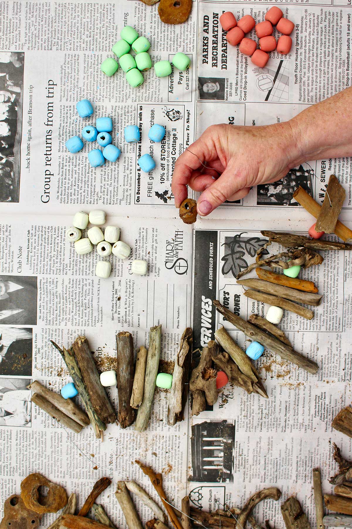 Person holding a piece of driftwood showing the hole in the center with painted wooden beads and a driftwood hanging in process.