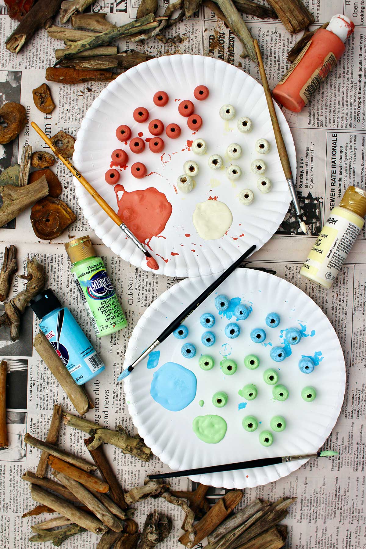 Paper plate with painted wooden beads drying with many pieces of driftwood scattered around it.