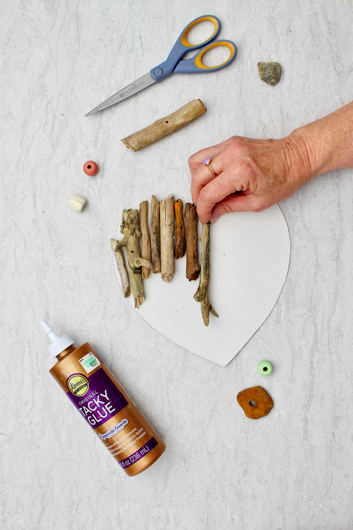 Person gluing small pieces of driftwood to a cardstock heart with tacky glue.