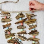 Person attaching a third driftwood garland to a driftwood stick for hanging.