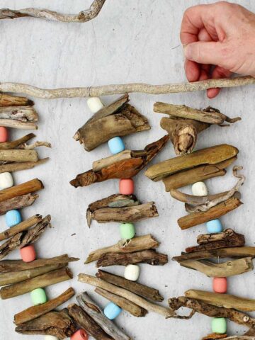 Person attaching a third driftwood garland to a driftwood stick for hanging.