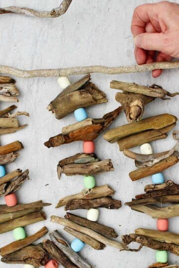 Person attaching a third driftwood garland to a driftwood stick for hanging.