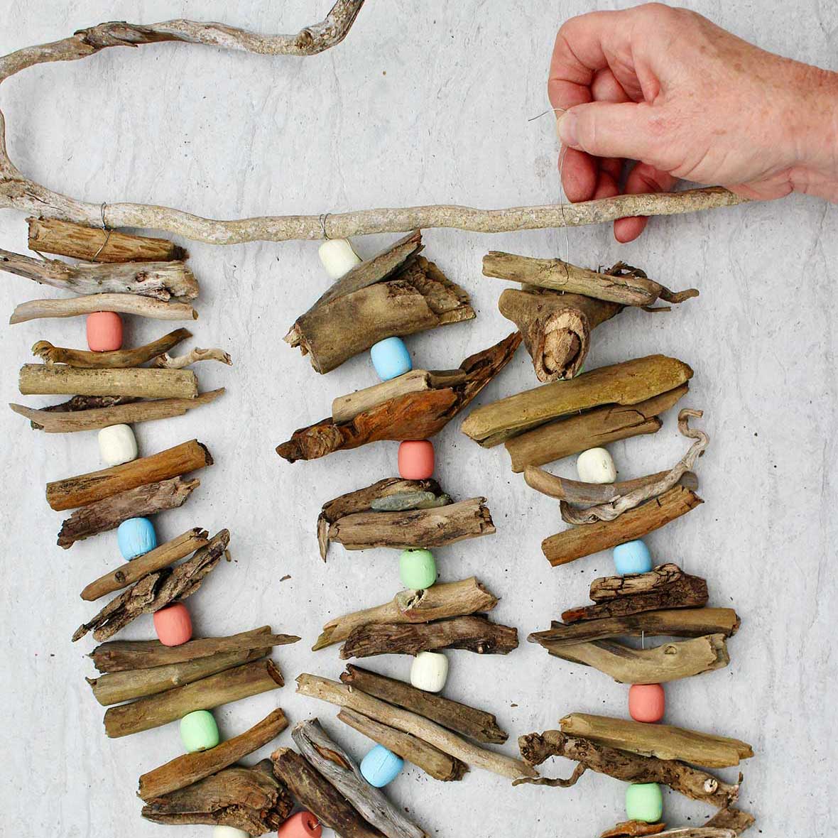 Person attaching a third driftwood garland to a driftwood stick for hanging.