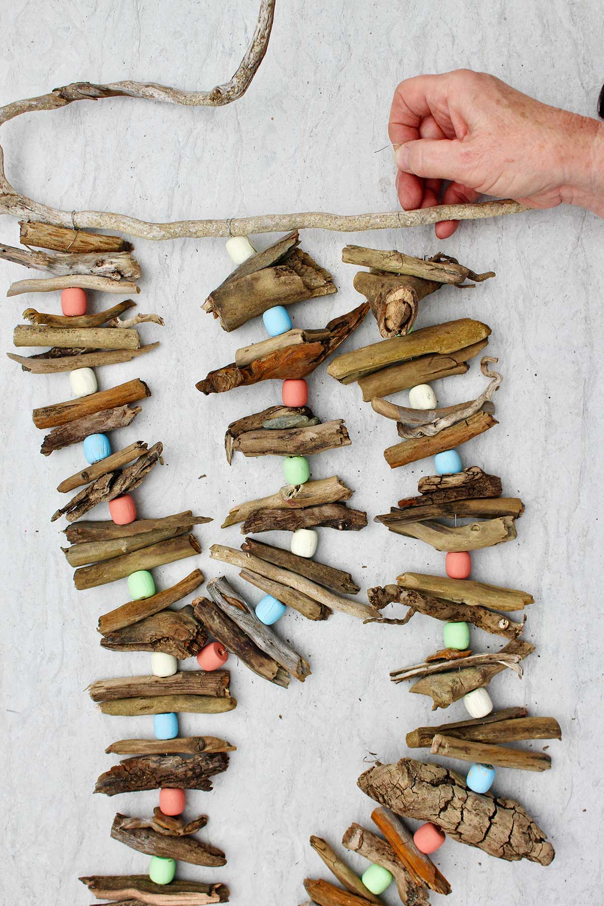 Person attaching a third driftwood garland to a driftwood stick for hanging.