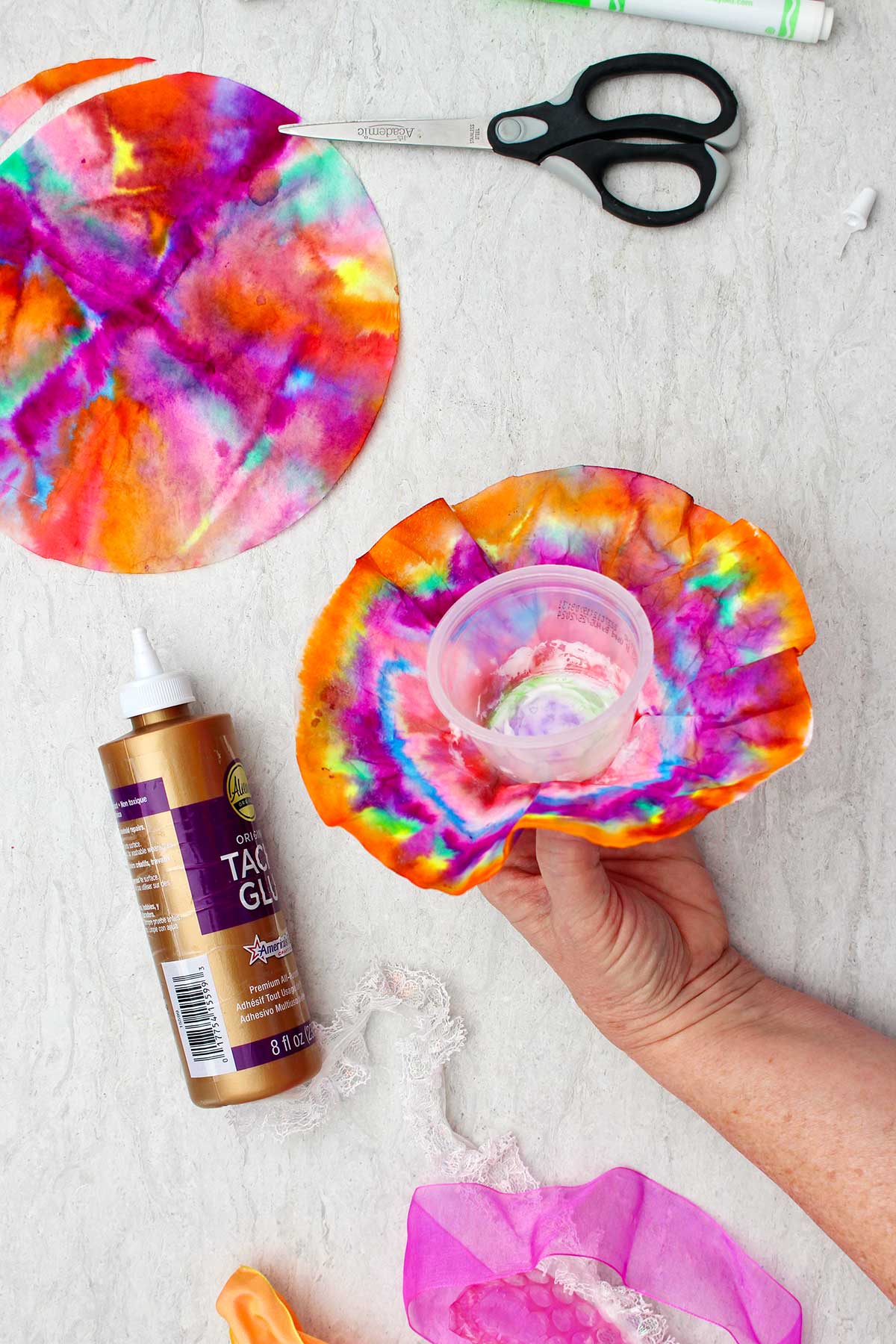 Person attaching plastic cup to colored coffee filter with other supplies near by.