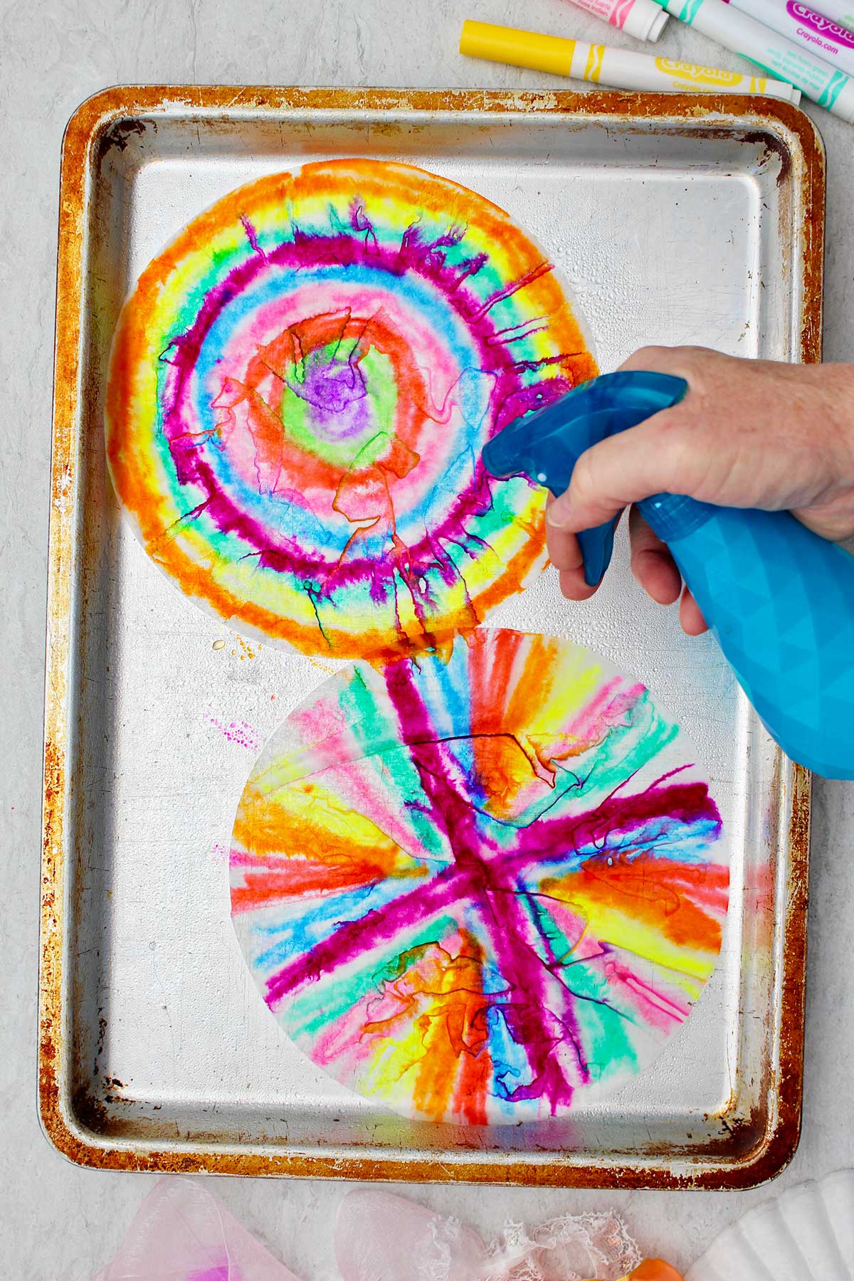 Person spraying colored coffee filters with water on a metal cookie sheet.