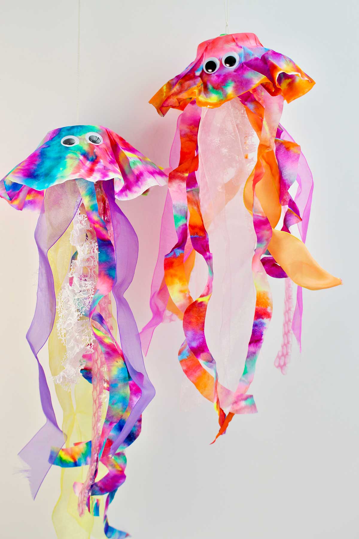 Pink, purple and orange coffee filter jellyfish with googly eyes and another jellyfish made with more jewel toned colors.