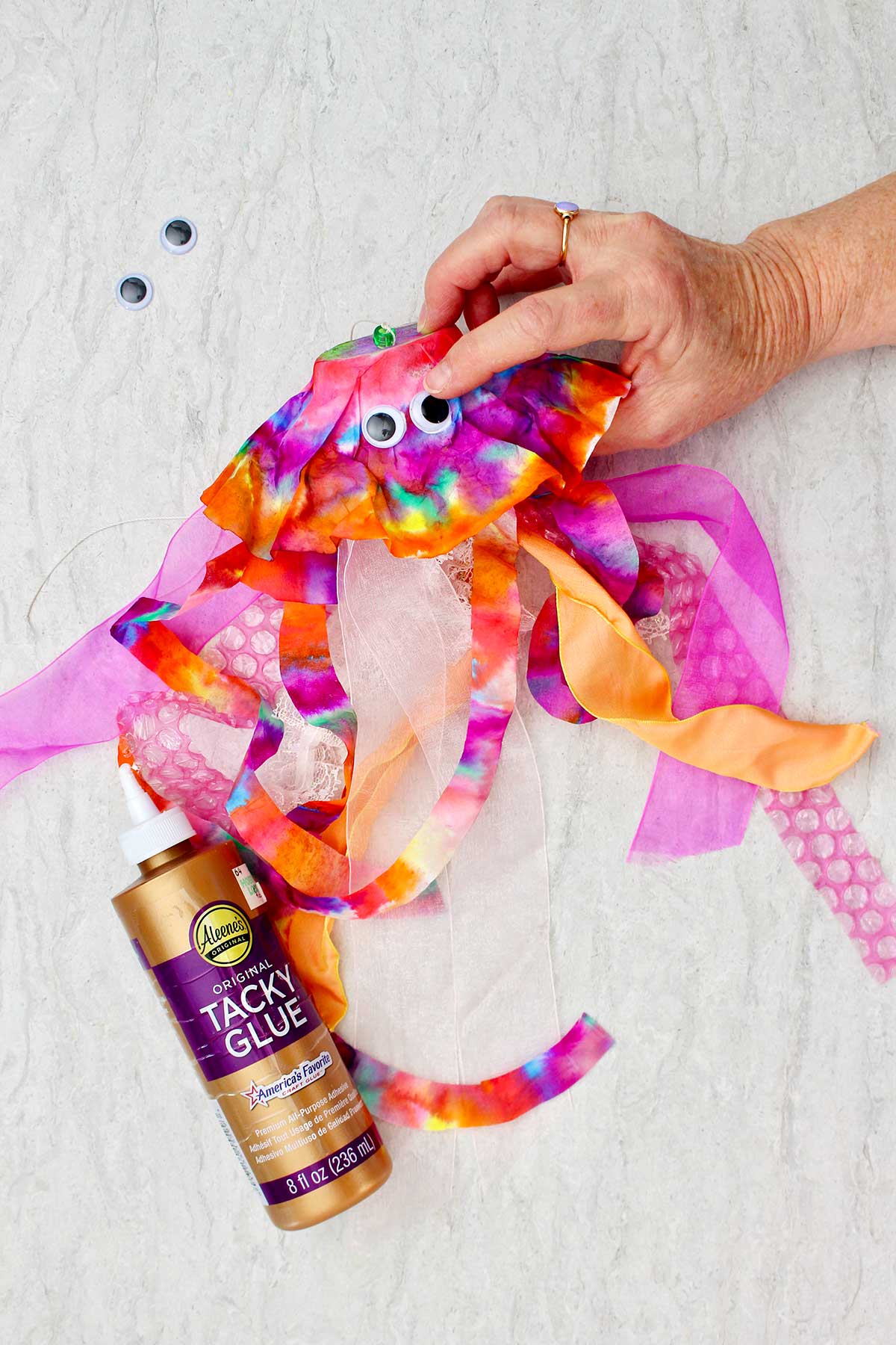 Person attaching googly eye to almost completed jellyfish.