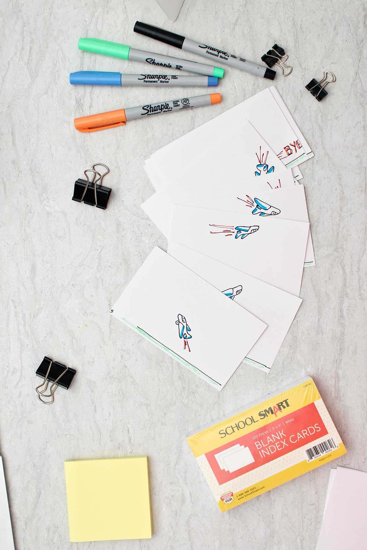 Multiple index cards with sketches of airplanes in different directions with colorful sharpies, binder clips, index cards and post it notes near by.