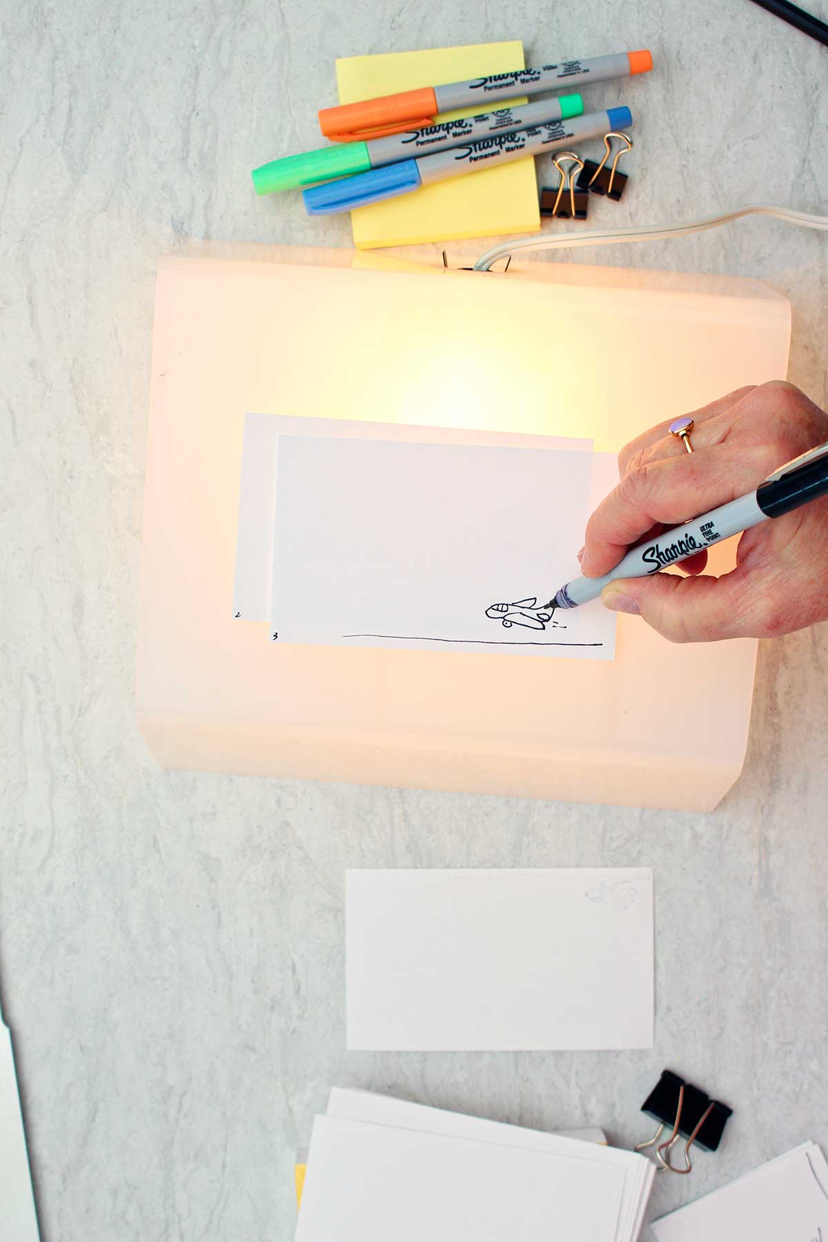 Person sketching a picture of an airplane on a numbered index card on a light box.