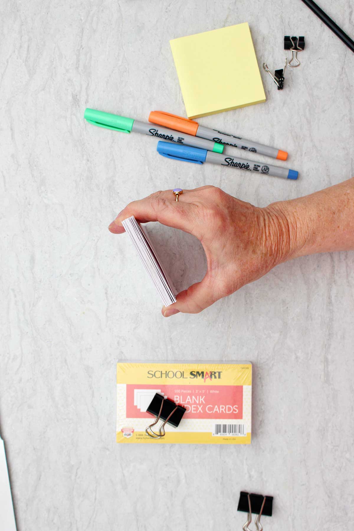 Person showing the camera the thickness of the stack of index cards with colorful sharpies and other supplies near by.