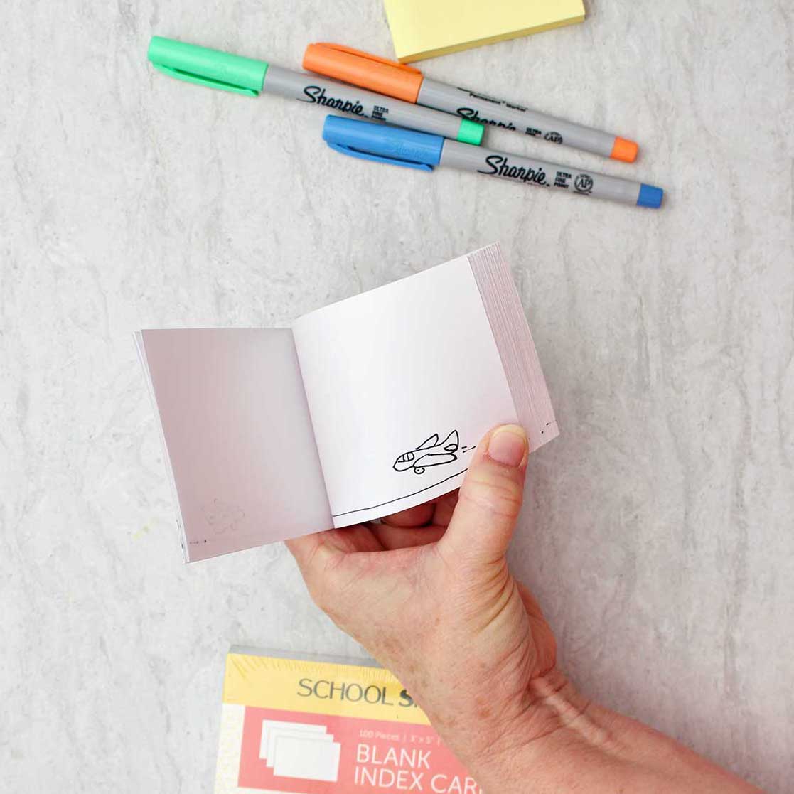 Person holding flip book showing movement of airplane sketch with colorful sharpies and other supplies near by.