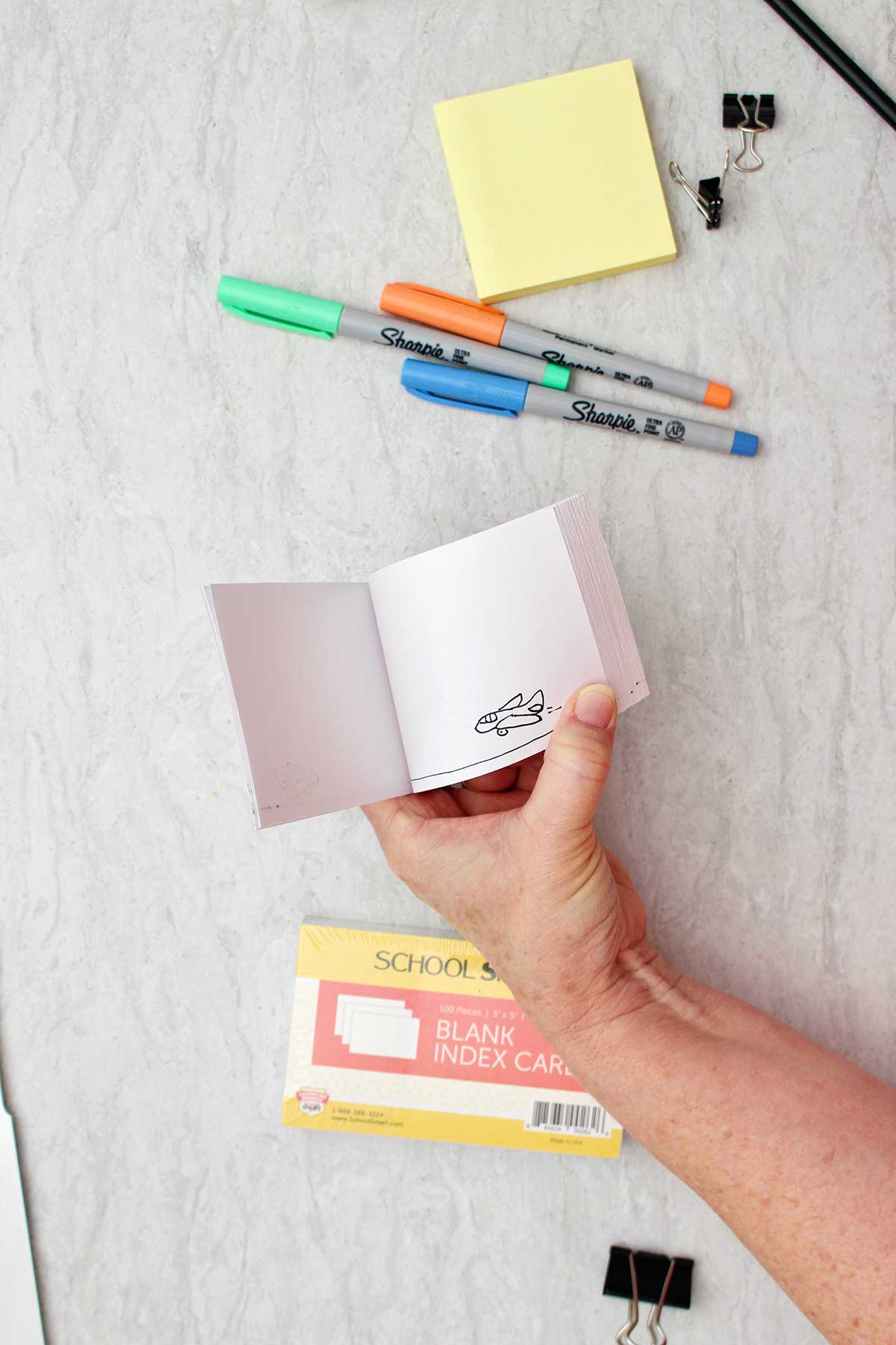 Person holding flip book showing movement of airplane sketch with colorful sharpies and other supplies near by.