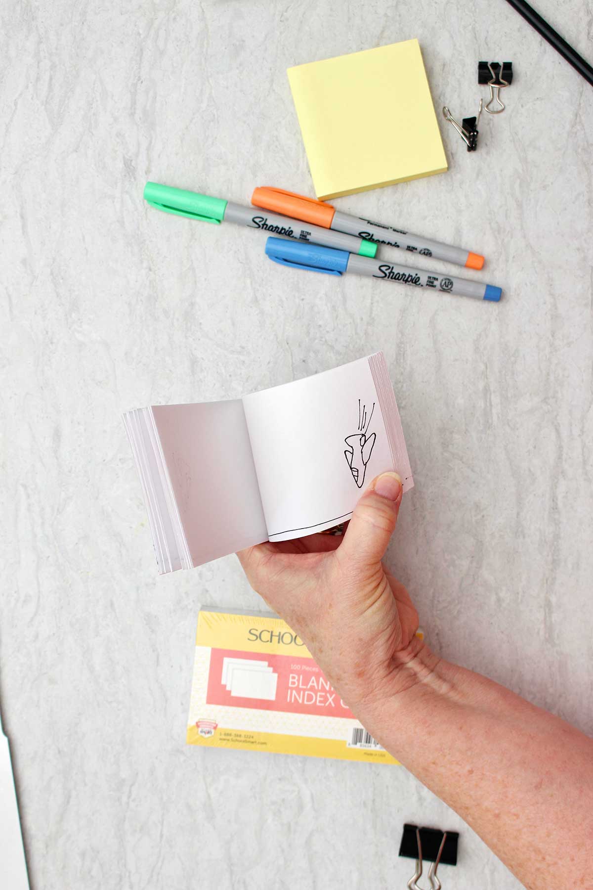 Person holding flip book showing movement of airplane sketch with colorful sharpies and other supplies near by.