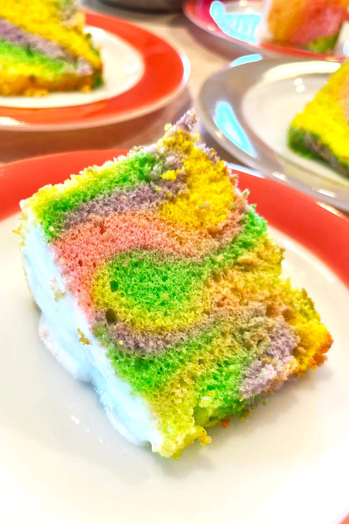 A piece of color swirled angel food cake sitting on a red and white plate.