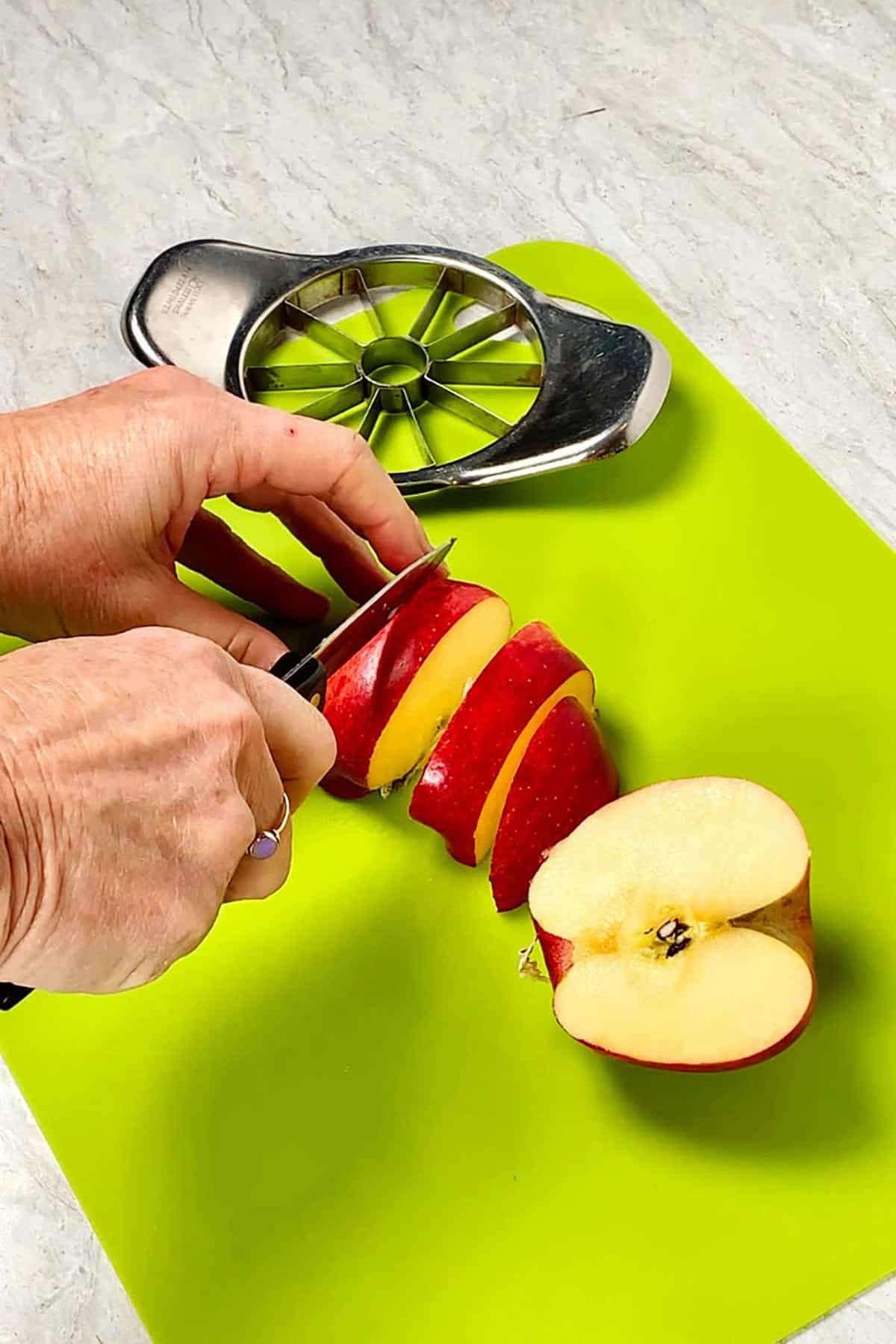 Person slicing apples with a knife on bright green cutting board.