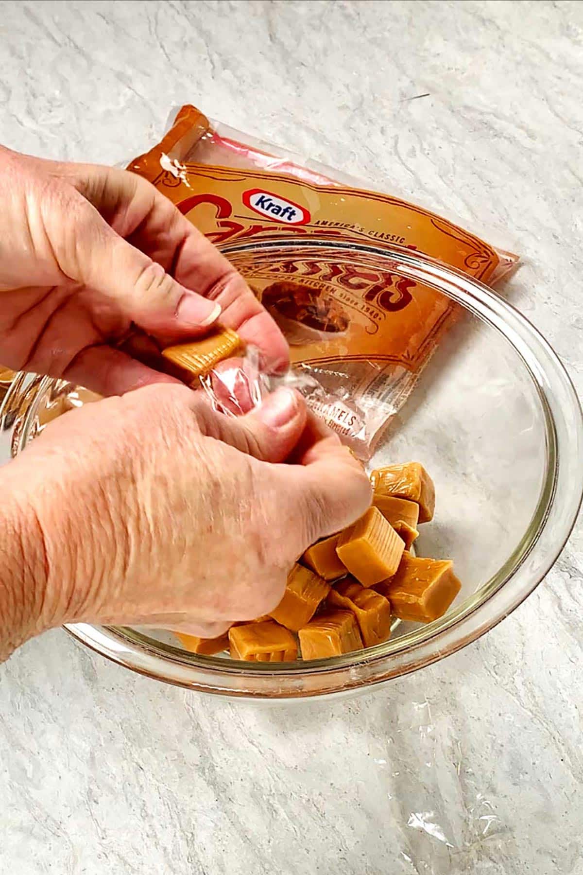 Person unwrapping Kraft Caramels into glass bowl.