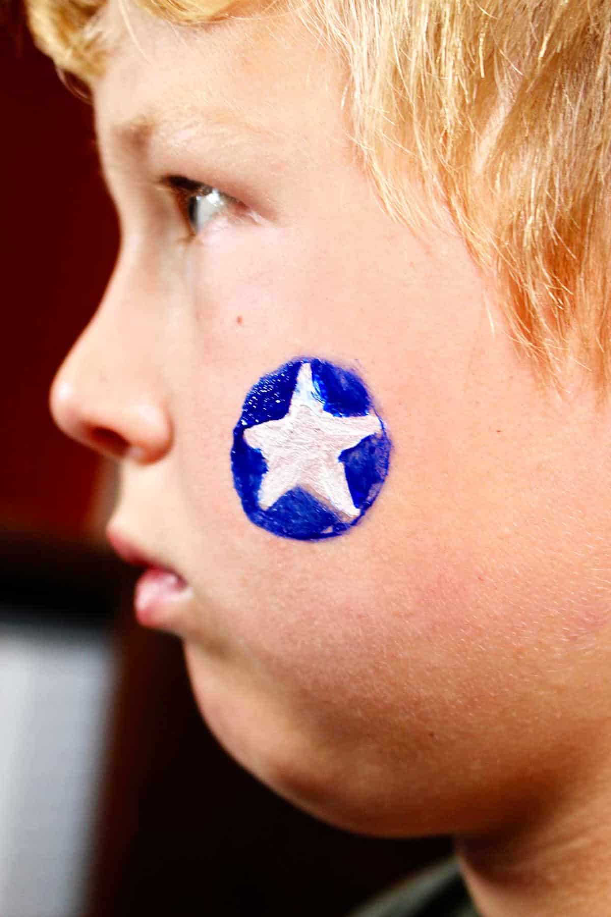 Profile of boy with blue circle with white star painted on cheek.