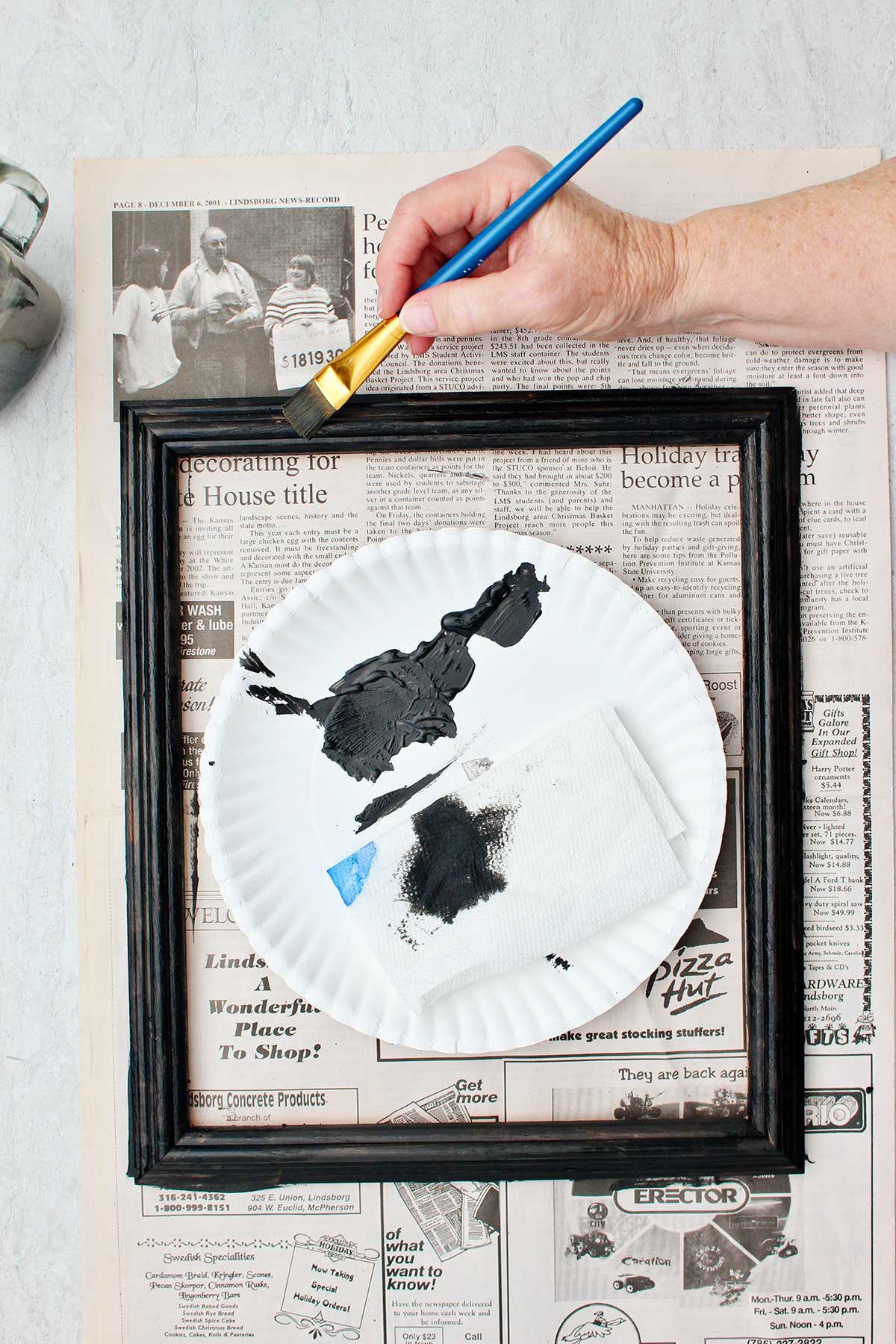 Person painting picture frame black on a piece of newsprint.