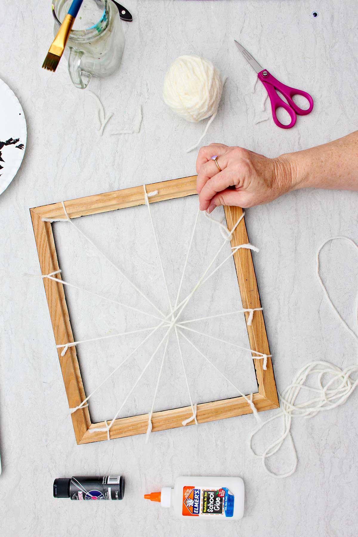 Person showing the back of the picture frame where all the yarn pieces are tied to make the base of the spider web.