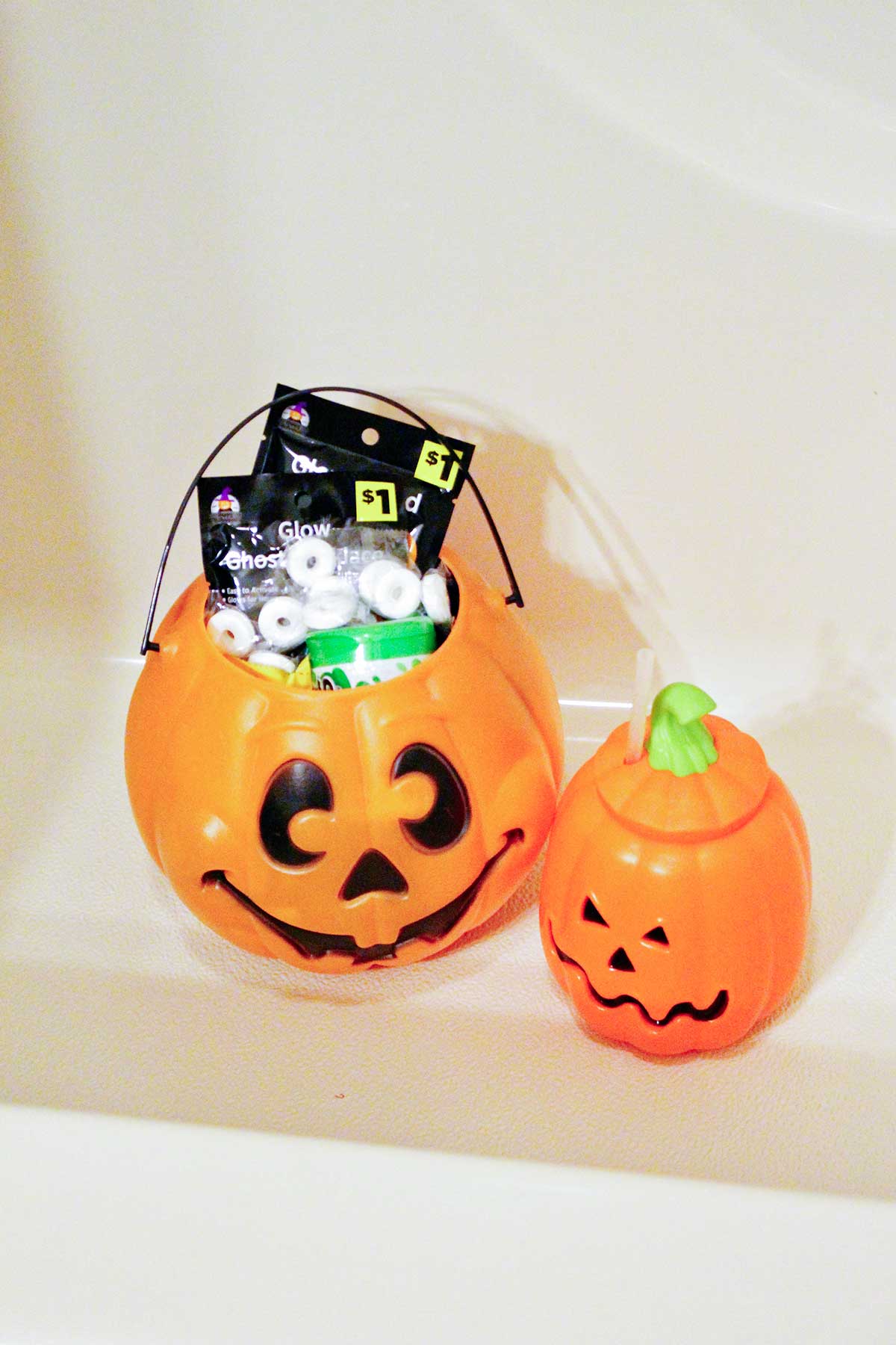 Two plastic jack-o-lantern candy buckets sitting in the bottom of a tub.