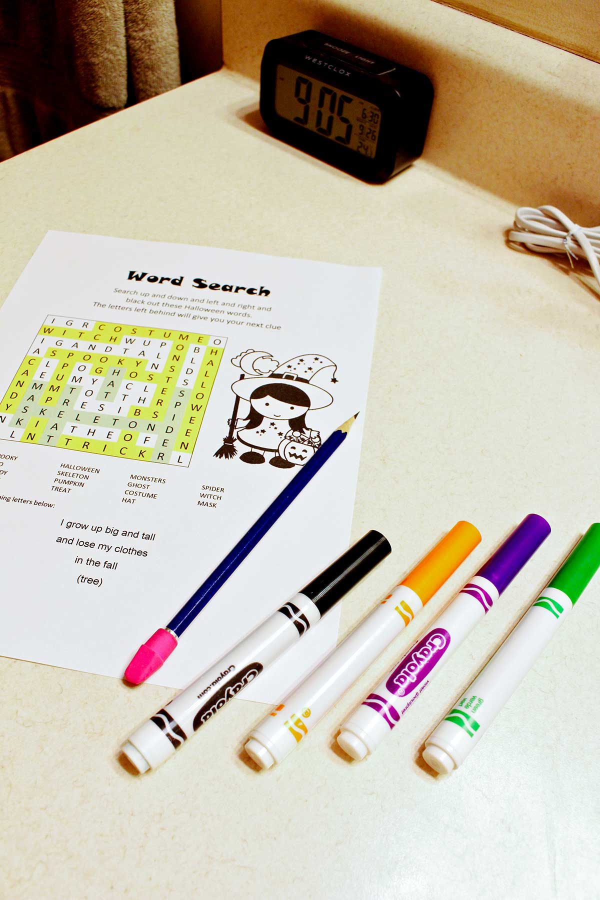 A scavenger hunt word search, some markers and a pencil on a counter top.