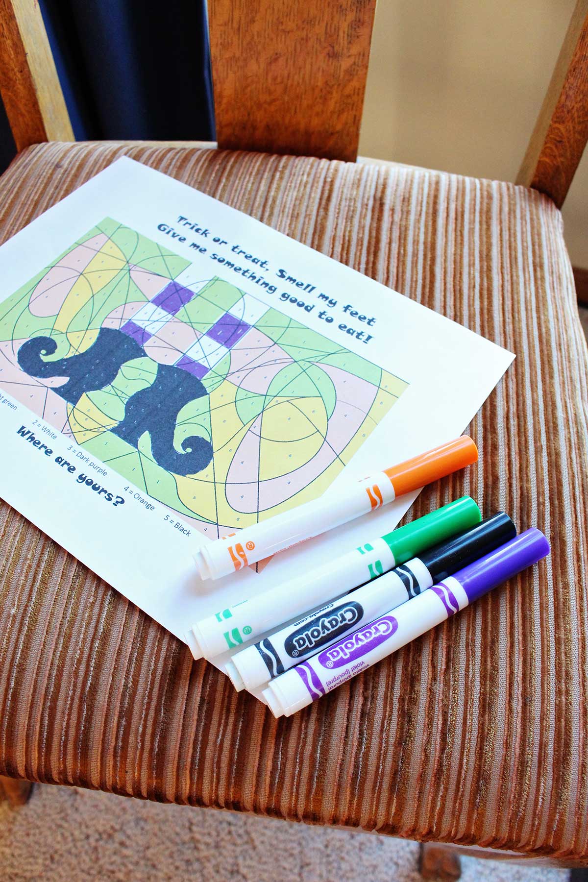 A colored scavenger hunt page sitting on a chair with some Crayola markers.