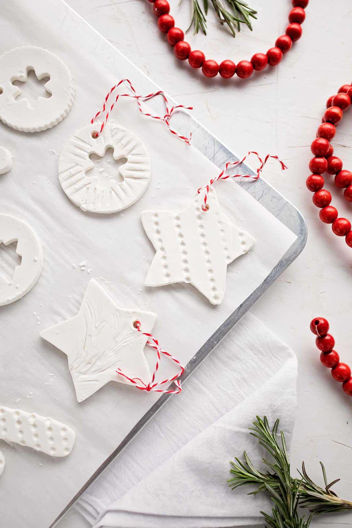 Cookie tray lined with parchment with completed ornaments resting on it. White linen, greenery and red wooden garland nearby.