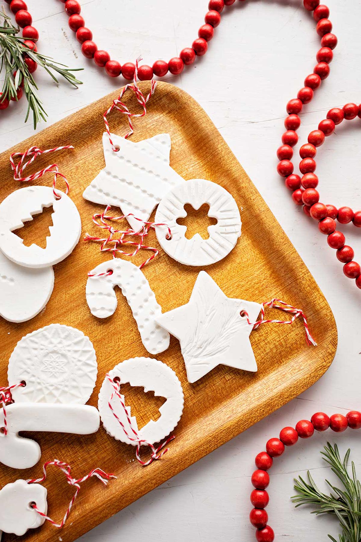 Wooden tray of completed cornstarch ornaments with red wooden garland and greenery nearby.