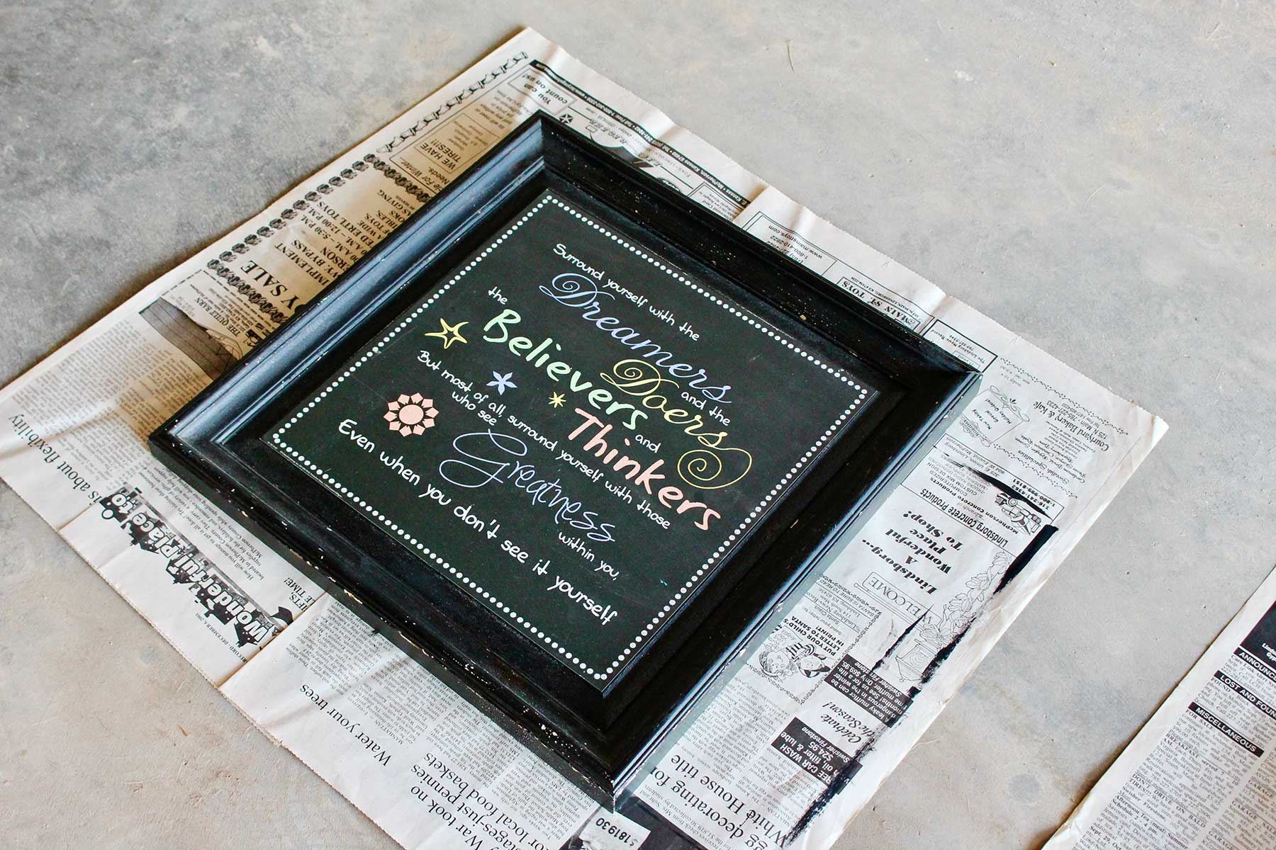 Black framed quote laying on newsprint, ready for spray paint.