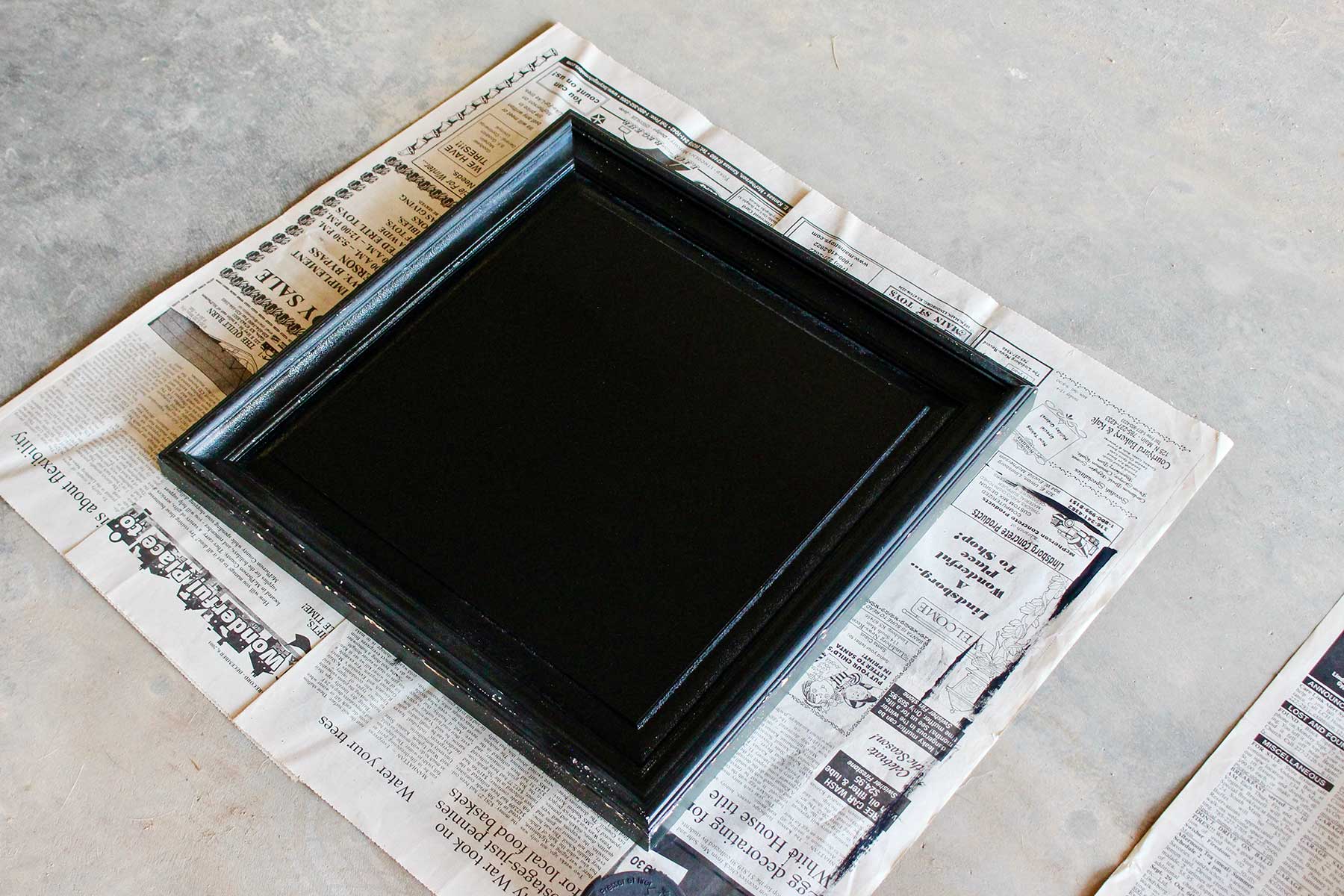 Spray painted black framed DIY chalkboard drying on a piece of newsprint.