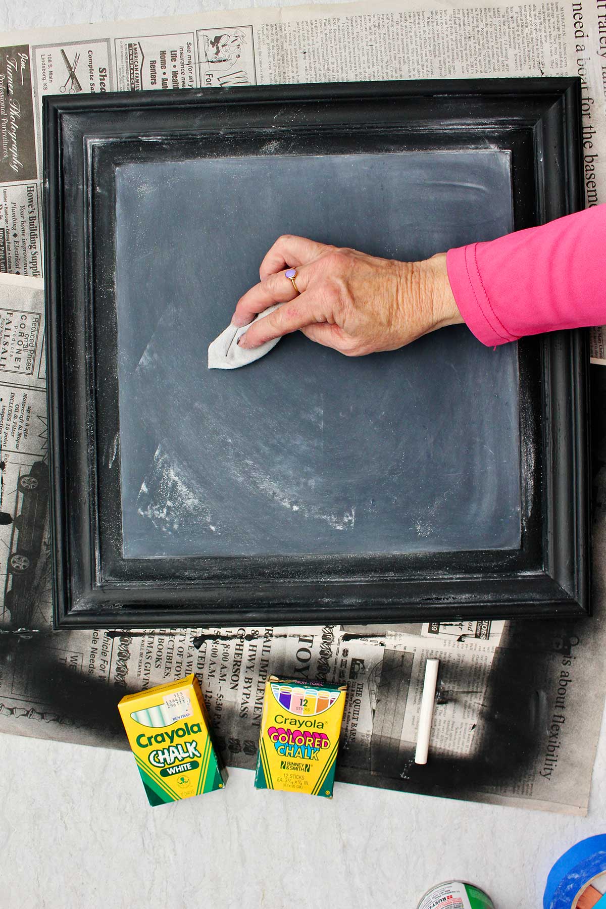 Person with pink shirt wiping chalk away to make a good base for the DIY chalkboard sign.