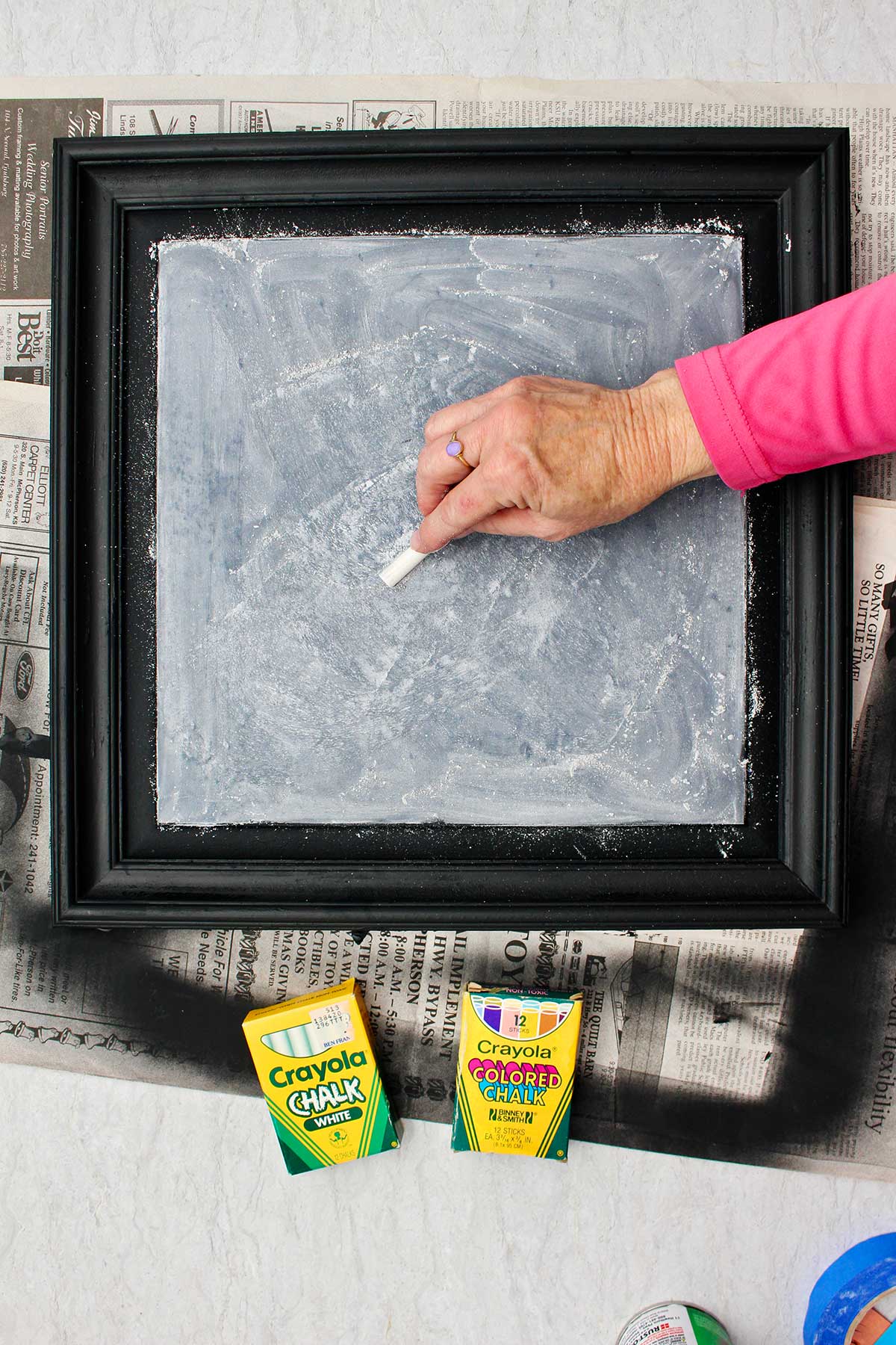 Person with pink shirt coloring chalk all over the surface of the DIY chalkboard to make a good base.