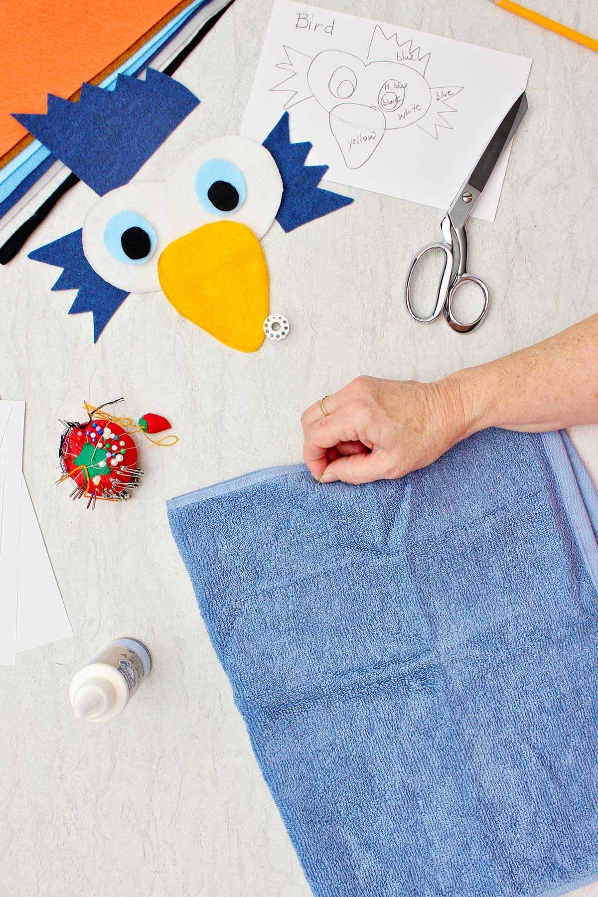 Person pinning blue terrycloth towel for bird costume with other pieces of the costume near by.