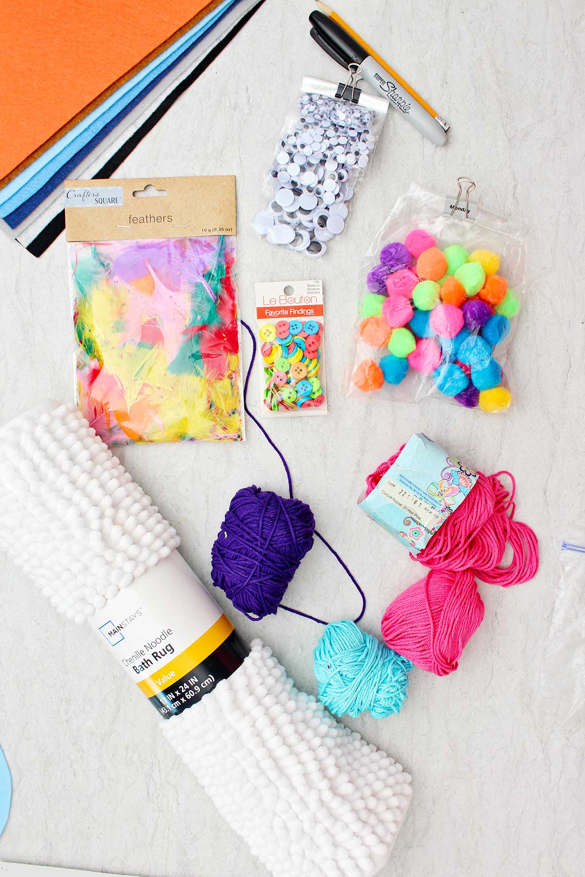 Items for making DIY Halloween costumes. Googly eyes, feathers, pompoms, colored string, buttons and a white bath mat.