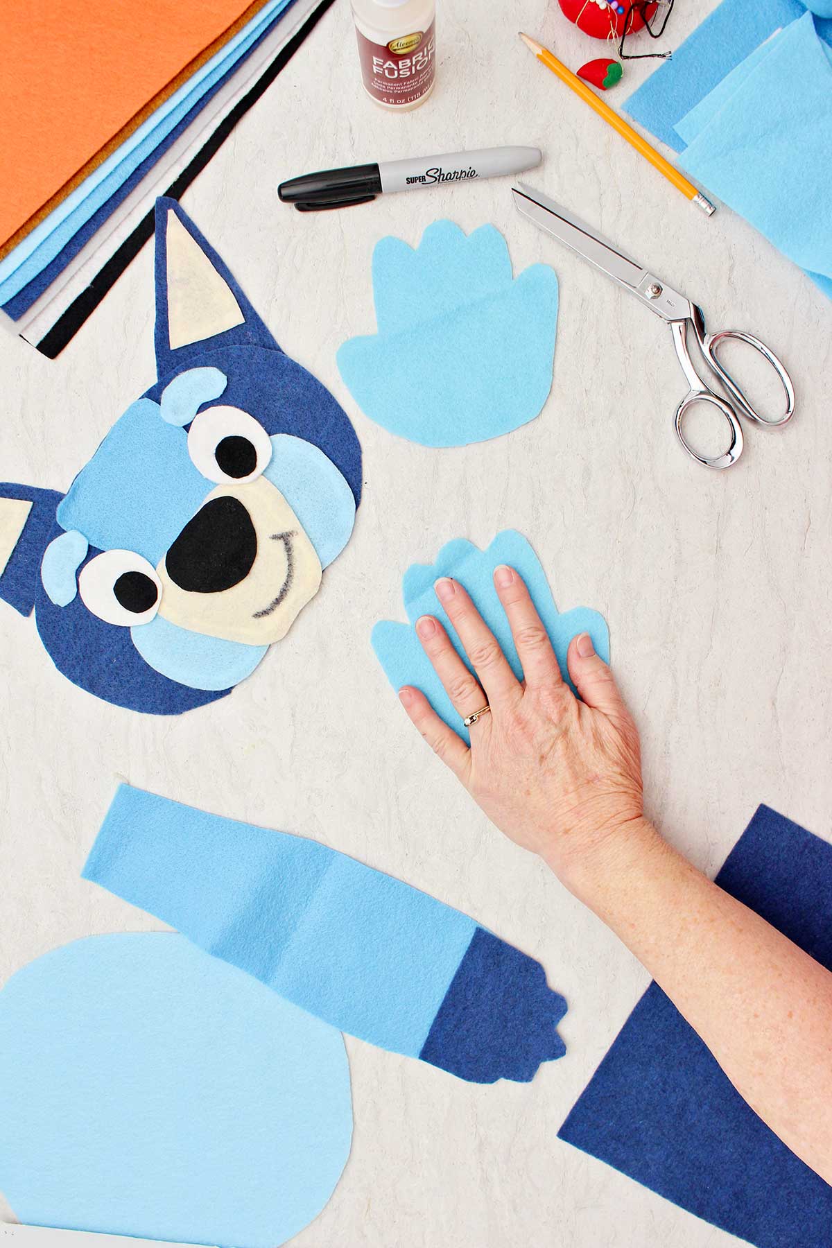 Person measuring their hand to make a blue paw for the Bluey costume with other pieces of the costume near by.