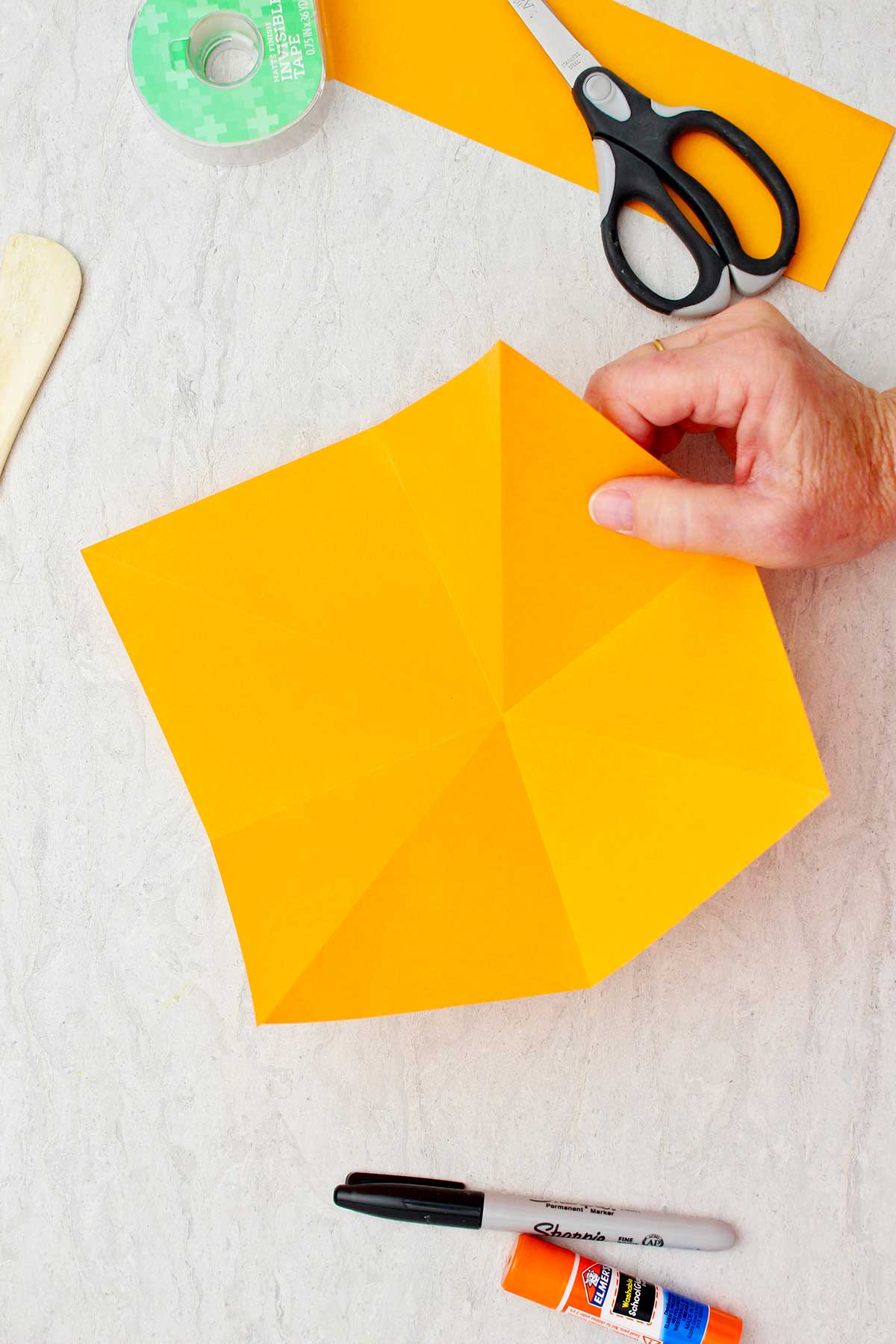 Hand holding the right side of a cut piece of orange paper ready for folding into an origami pumpkin.